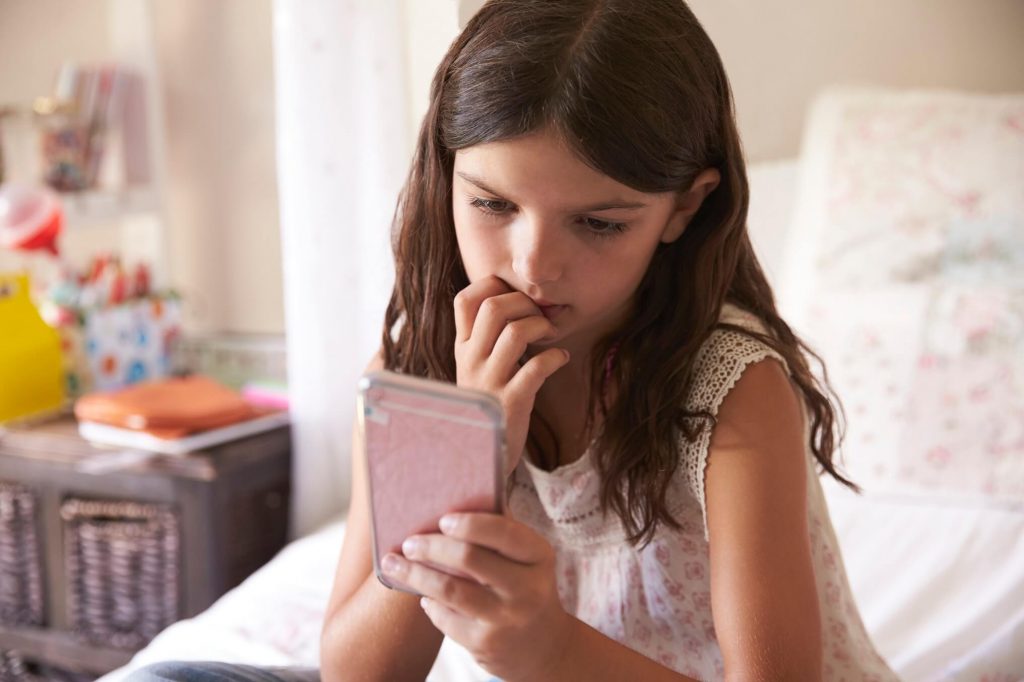 young girl in bedroom worried by cyber bullying text message