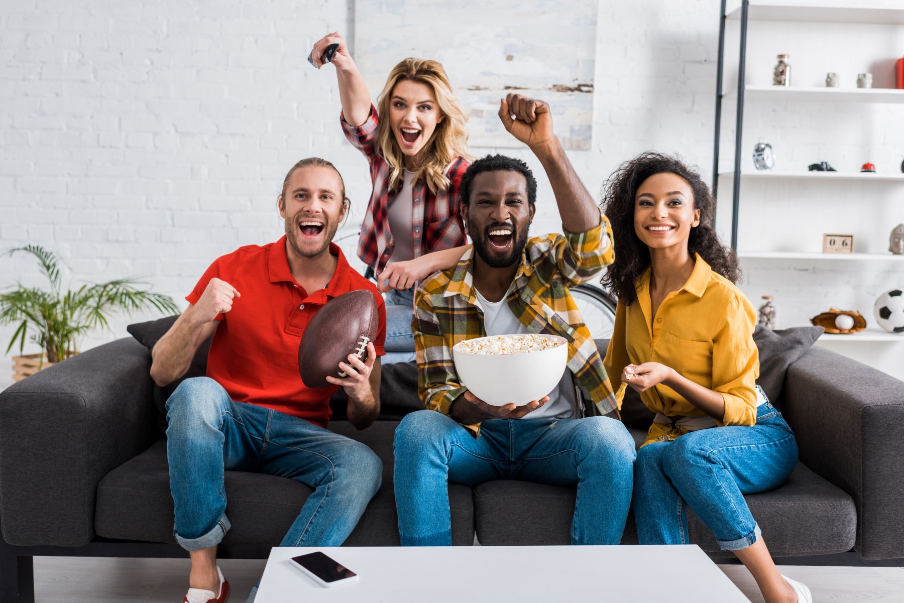 happy multi-ethnic friends sitting on couch watching live sports