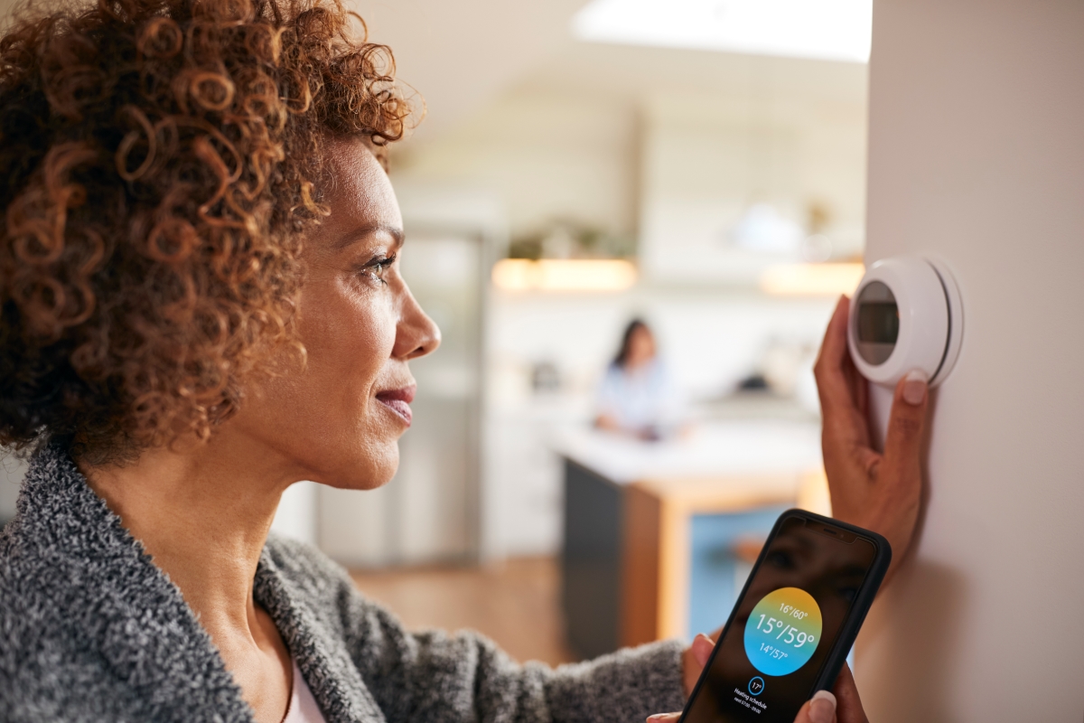 mature-woman-using-app-on-phone-to-control-digital-thermostat